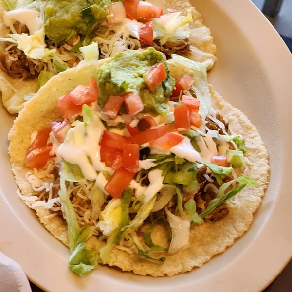 Two Freedom Burrito tostadas topped with meat, lettuce, cheese, tomatoes, sour cream, and guacamole.