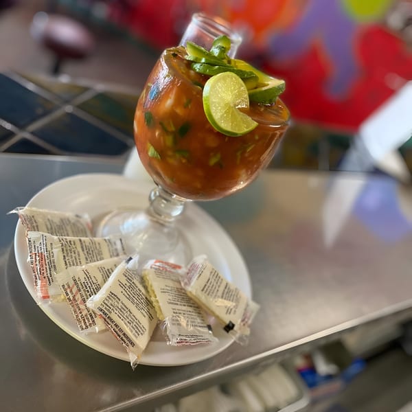 A large glass of Mexican shrimp cocktail, garnished with lime and avocado, on a white plate with crackers.