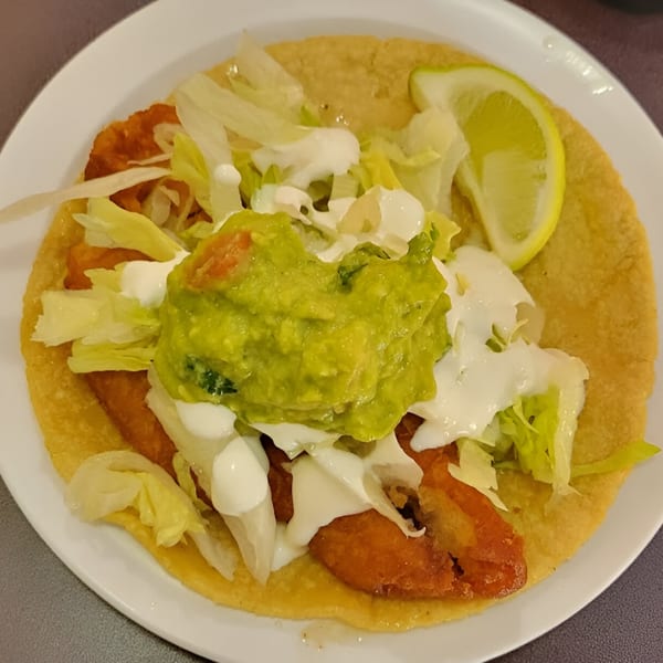 A Freedom Burrito fish taco with guacamole, sour cream, lettuce, and a lime wedge on a white plate.