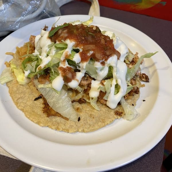 A Freedom Burrito tostada with chicken, lettuce, sour cream, and salsa on a white plate.